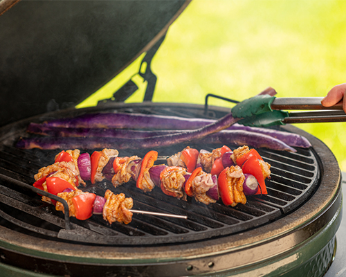 kamadogrillen mit gemuesespiess und gegrillter melanzani bedient mit einer edelstahlzange und einer hand fuer den Kamadogriller