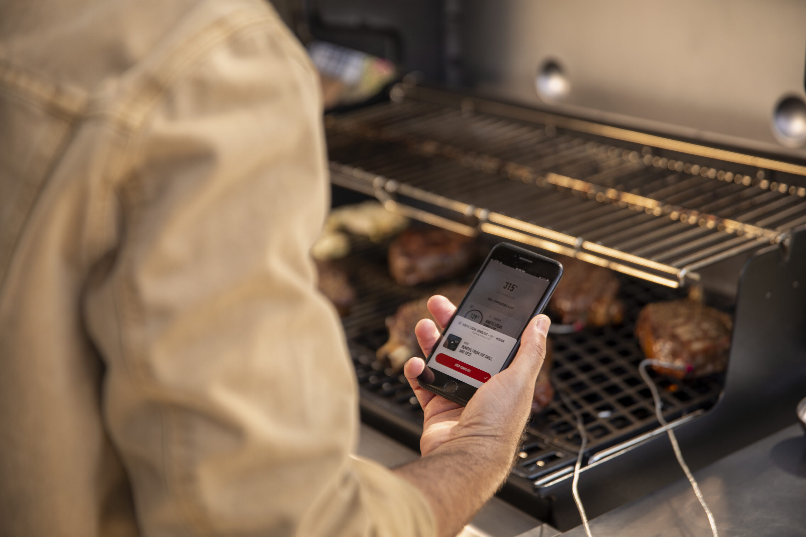 Mann am Grill mit Temperaturmesser auf der Handyapp